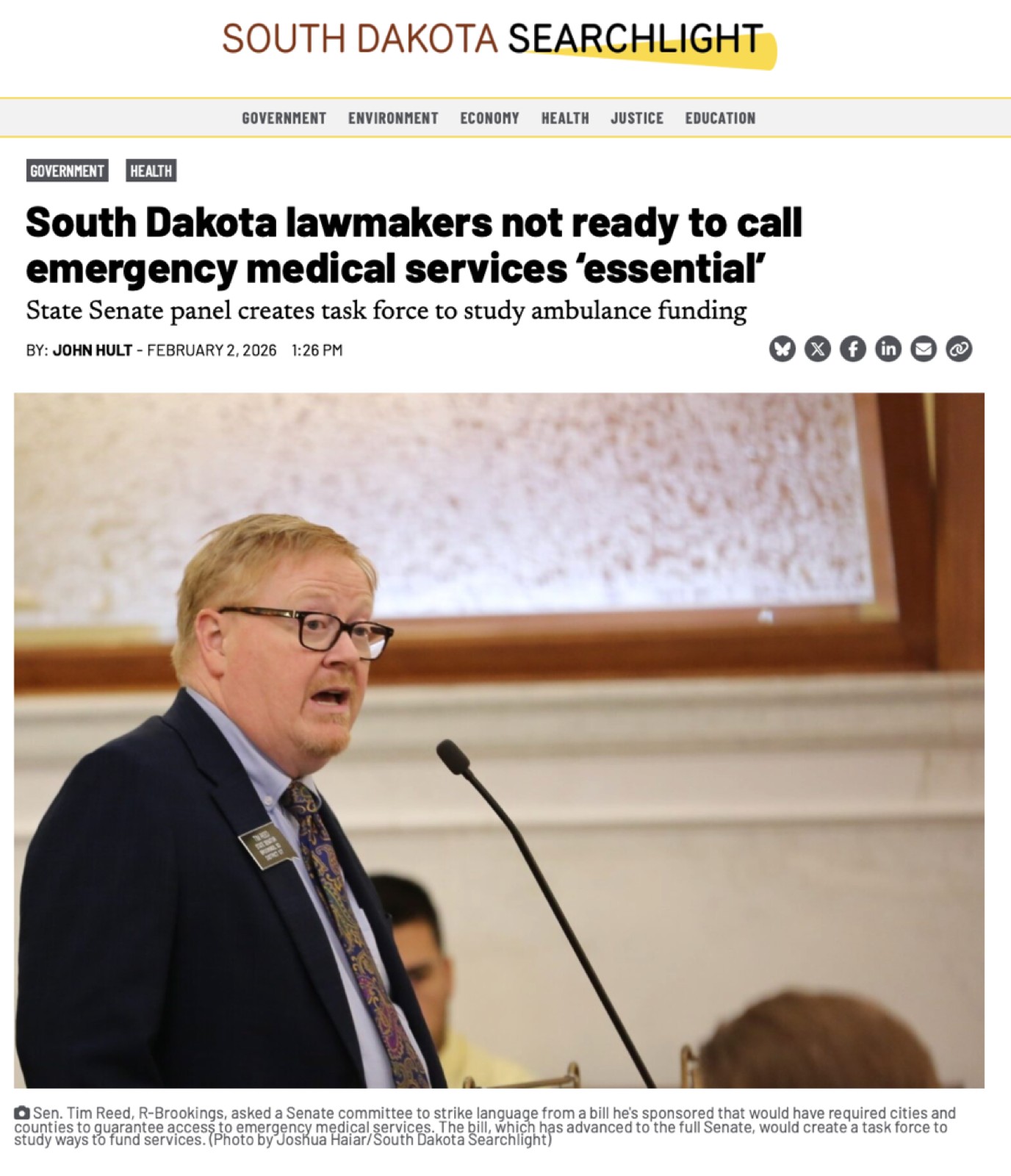 Screenshot of a South Dakota Searchlight news article headlined 'South Dakota lawmakers not ready to call emergency medical services essential,' showing State Senator Tim Reed speaking at a podium on February 2, 2026.