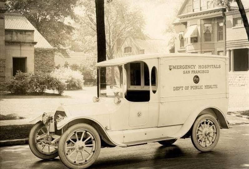 An early white motor ambulance lettered Emergency Hospitals, San Francisco, Dept of Public Health, parked on a residential street