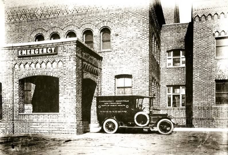 Park Emergency Hospital, a brick building marked EMERGENCY, with an early motorized San Francisco Department of Public Health ambulance parked outside